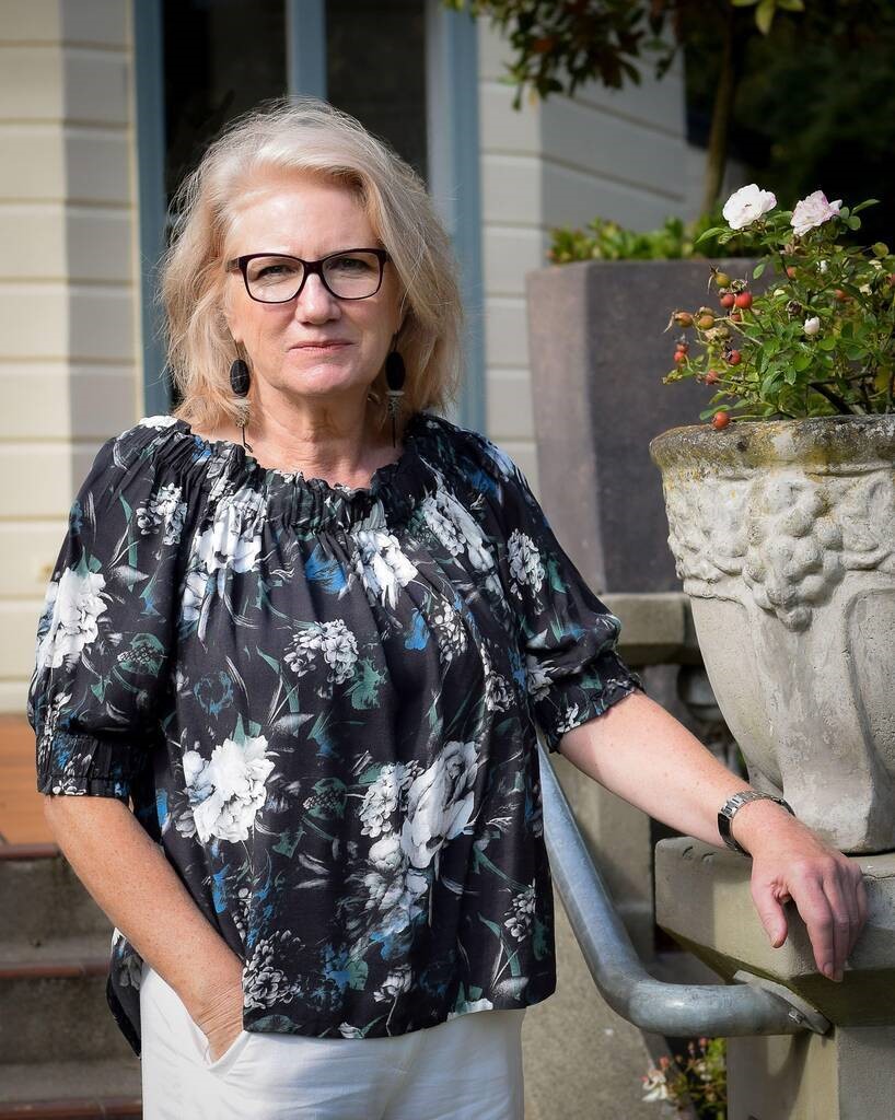 Woman with glasses and floral top standing on step.