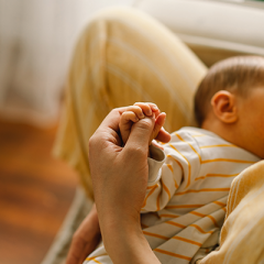 woman breasfeeding baby while holding it's hand