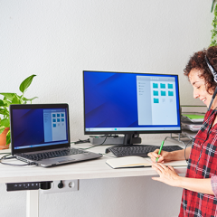 Woman writing in notepad at a standing desk with headphones on. 