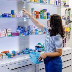 A female pharmacy student in a pharmacy setting reaching for medication on a shelf