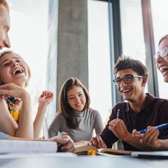 Students happily chatting and laughing together while seated at a table.