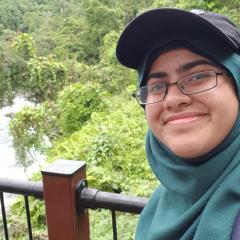Woman with green scarf and glasses standing in front of waterfall.