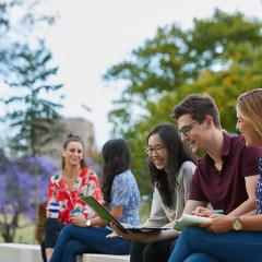 A group of students sitting on a bench looking at a laptop. 