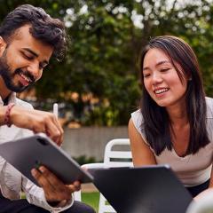 Two students sit comparing notes on tablets in Alumni Court at UQ's St Lucia campus