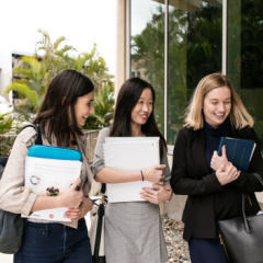 Three female presenting students walking with laptops and notebooks