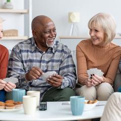 a diverse group of elderdly men and women enjoying a game of cards with coffee and snacks