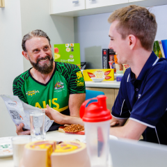 Two men at a table with a laptop and food, engaged in conversation and collaboration.