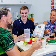 A man and woman enjoy a meal together at a table, sharing a box of food and smiling at each other.