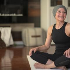 Woman smiling, sittinng on a yoga mat wearing a beanie hat