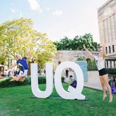 prospective students jumping for joy in front of a big UQ sign