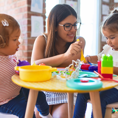 Young female childcare working playing with plastic toys with two young children