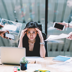 Woman stressed at work desk as people hold out more tasks for her to complete