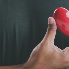 A plastic heart being held in front of a person's chest to signify self-compassion