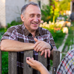 Man leaning on fence talking to neighbour smiling