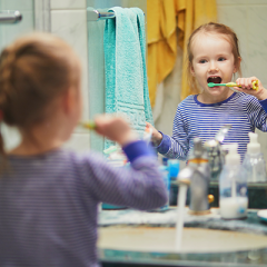 Young girl standing in front of mirror brushing teeth. 