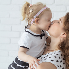 Mother kissing young  daughter with hearing device