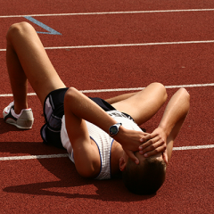 Competitive running athlete lying on ground with hands on face.