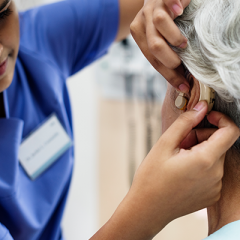 Aged care worker fitting hearing aid on resident