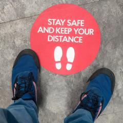 person's feet standing on a social distancing reminder sticker