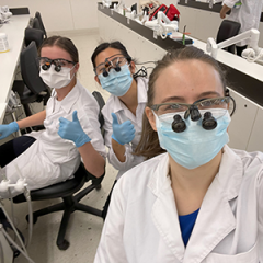 Gabrielle Starr wearing a lab coat in a dental lab with 2 other students