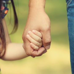 Close up image of a child and adult holding hands.