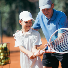 Coach guide young boy with tennis racquet