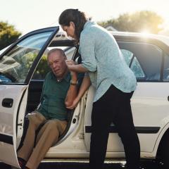 woman helping elderly man out of car 