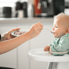 Mother feeding baby solid food in highchair 