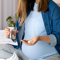 Pregnant woman holding pills in hand with glass of water