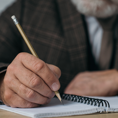 Elderly man writing in notebook with pencil