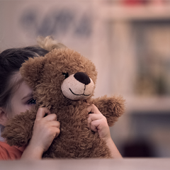young girl hiding face behind teddy bear